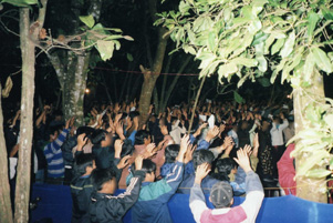 A group of believers is gathered outdoors. Most people have their hands raised.