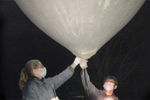 Two people are inflating a very large balloon during the night.