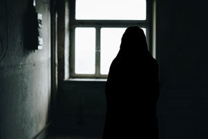 The silhouette of a young woman standing at a window.