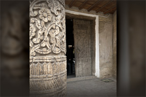 Entry to a building; a pillar with intricate carvings is in the foreground.