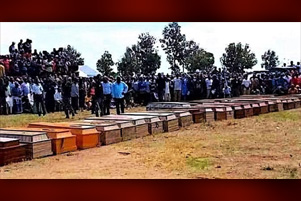 Line of coffins, with mourners gathered.