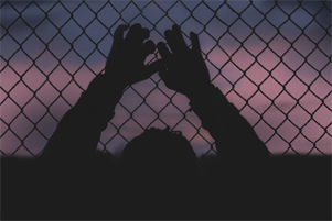 A silhouette of a man gripping a chain link fence.
