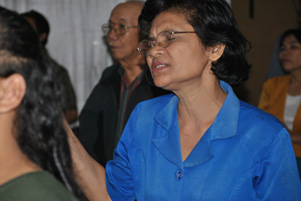 A woman is standing with her hands lifted and eyes closed. She is with a congregation.