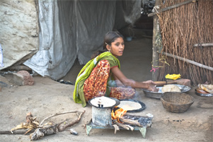 A young girl cooking over an open fire just outside her home.