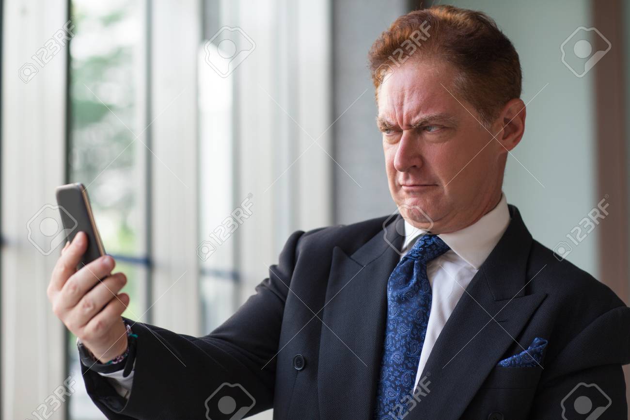 74740320-frowning-businessman-taking-selfie-on-mobile-phone.jpg